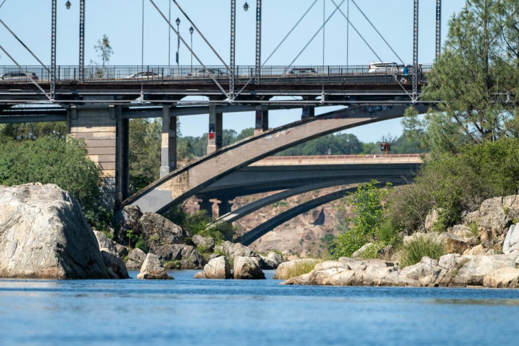 Folsom Tree Service | Image of trees along Folsom Lake, CA, with a bridge in the background and rocks and boulders in the water